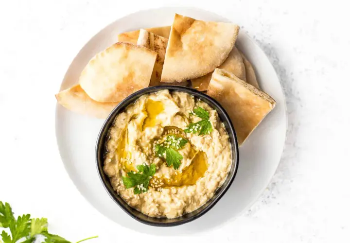 Un bol de caviar d'aubergine crémeux, garni d'huile d'olive, de persil et de sésame, servi avec des morceaux de pain pita.