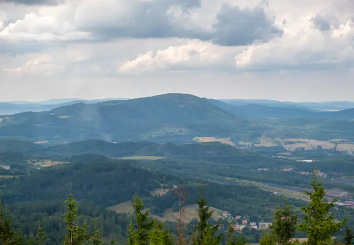 Widok na rozległą, zieloną dolinę z dominującą, zalesioną borową górą na horyzoncie. Na szczycie góry widoczna wieża telekomunikacyjna.