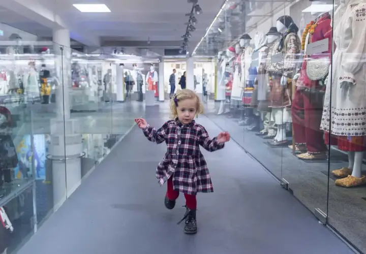 Mała dziewczynka biega po muzeum dla dzieci im. Janusza Korczaka, mijając gabloty z tradycyjnymi strojami.