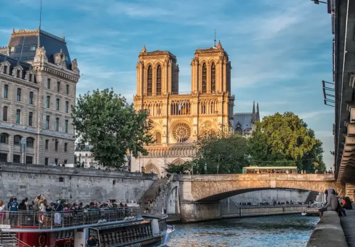 Katedra Notre Dame w Paryżu nad Sekwaną, z łodzią turystyczną i mostem w tle.