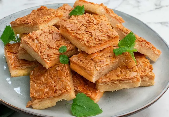 En hög med fyrkantiga bitar av en härlig mandelkaka, perfekt för ett "baka i långpanna deluxe recept". Garnerad med mynta.