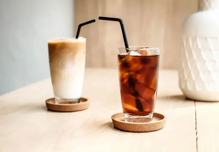 Zwei Gläser mit Eiswürfeln und Strohhalmen. Eines ist ein cremiger Eiskaffee, das andere ein dunkler Kaffee mit kaltem Wasser.