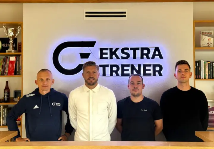 Czterech mężczyzn stoi przed podświetlanym logo "EKSTRA TRENER". Dwóch z nich to srodkowy pomocnik, który jest trenerem.