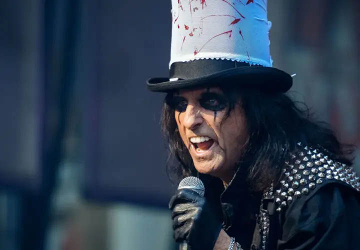 Alice Cooper w Polsce, w swoim charakterystycznym makijażu i z kapeluszem, śpiewa do mikrofonu.