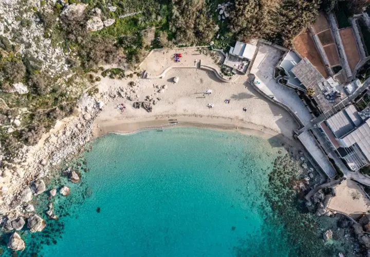 Widok z lotu ptaka na rajską zatokę na Malcie, z turkusową wodą, piaszczystą plażą i budynkami przy brzegu.