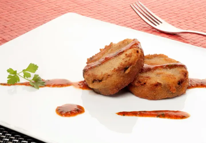 Dos manitas de cerdo rebozadas y fritas, servidas con salsa roja y perejil en un plato blanco.