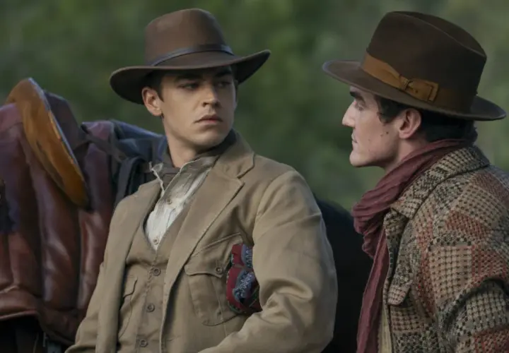 Två unga män i hattar och tidstypiska kläder, en med en sadel bredvid sig. Kanske en ung Sherlock Holmes på ett äventyr.