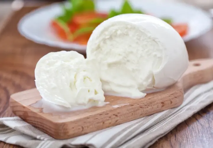 Świeża kulka mozzarelli na desce, w tle sałatka. Zastanawiasz się, ile kcal ma kulka mozzarelli?