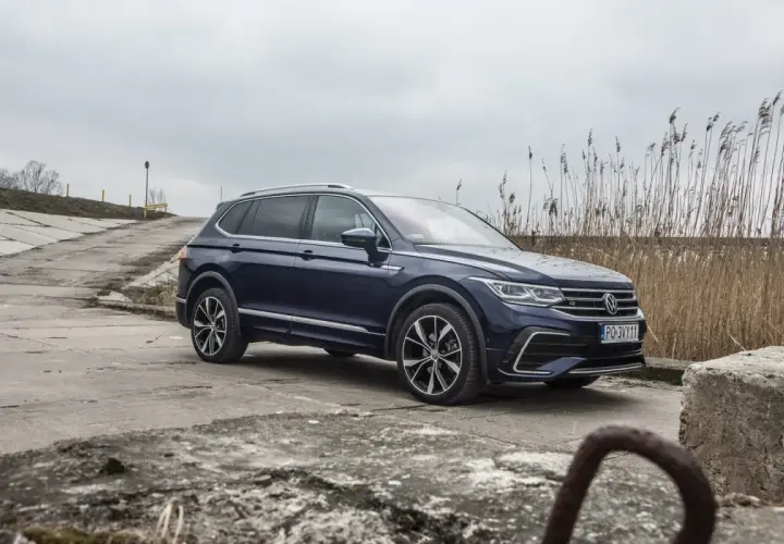 Ciemnoniebieski Volkswagen Tiguan Allspace na betonowej drodze, w tle trzciny i pochmurne niebo.