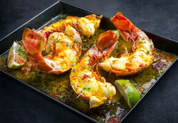 Langoustes grillées sur plancha, nappées d'une sauce verte et garnies de quartiers de citron vert et de thym.