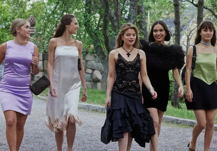Fyra unga kvinnor i eleganta klänningar, som barracuda queens, promenerar utomhus.