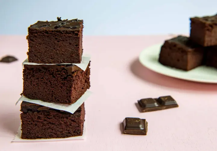 Ciemne, wilgotne brownie z fasoli ułożone w wieżę, obok kawałki czekolady.