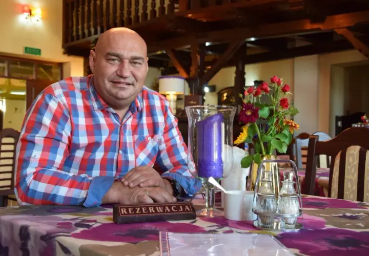 Łysy mężczyzna w kratę siedzi przy stole z kwiatami i świecą.
