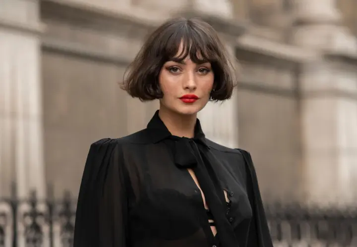 Eine Frau mit einem lässigen, **choppy bob** und rotem Lippenstift trägt eine transparente schwarze Bluse.