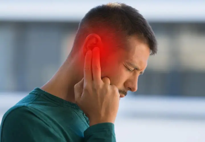Hombre con dolor de oído, señalando la zona afectada con un halo rojo. Podrían ser sabañones en las orejas.