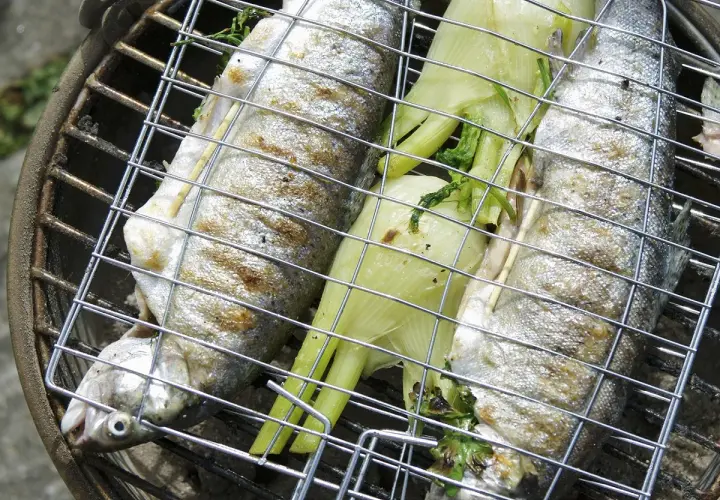 Trois truites au barbecue, garnies d'herbes et de fenouil, grillent sur un barbecue.