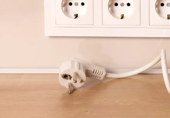 Biała wtyczka typu F leży obok gniazda elektrycznego na drewnianym blacie.