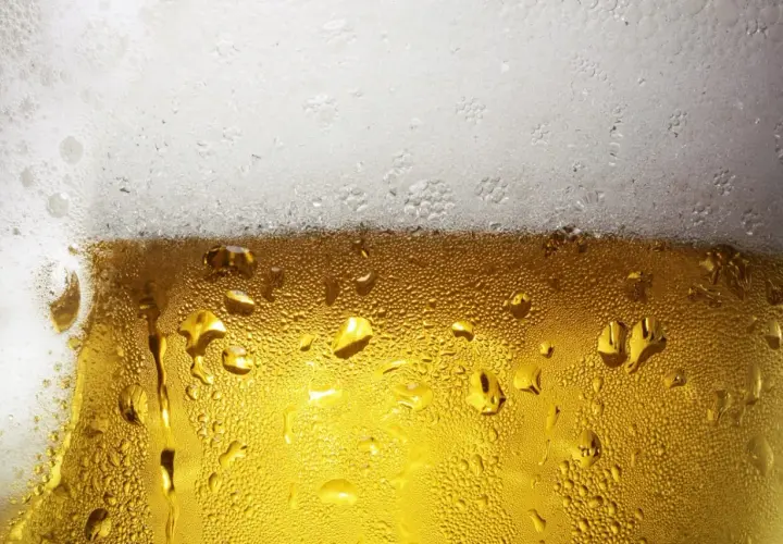 Zbliżenie na szklankę piwa z kroplami kondensacji i białą pianką na górze.