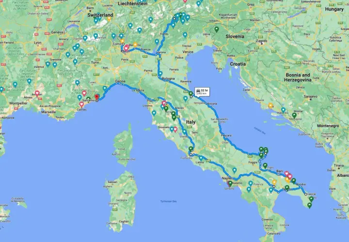 A winding blue line traces a scenic Italy road trip route from the French border, through the Alps, down the Italian peninsula, and across to Sicily.