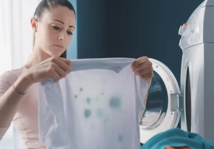Kobieta z niedowierzaniem patrzy na poplamioną koszulkę, która wyszła z pralki.