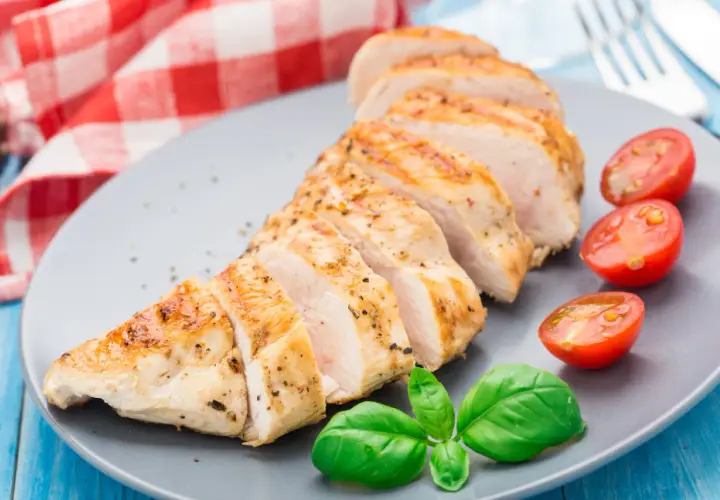 Tranches de blanc de poulet grillé, assaisonné de poivre et d'herbes, servi avec des tomates cerises et du basilic frais.