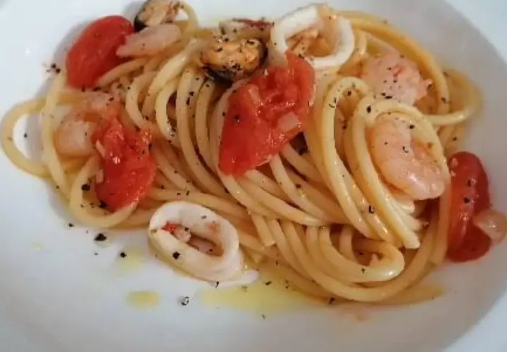 Pyszne spaghetti z owocami morza: krewetki, małże i kalmary w sosie pomidorowym z ziołami.