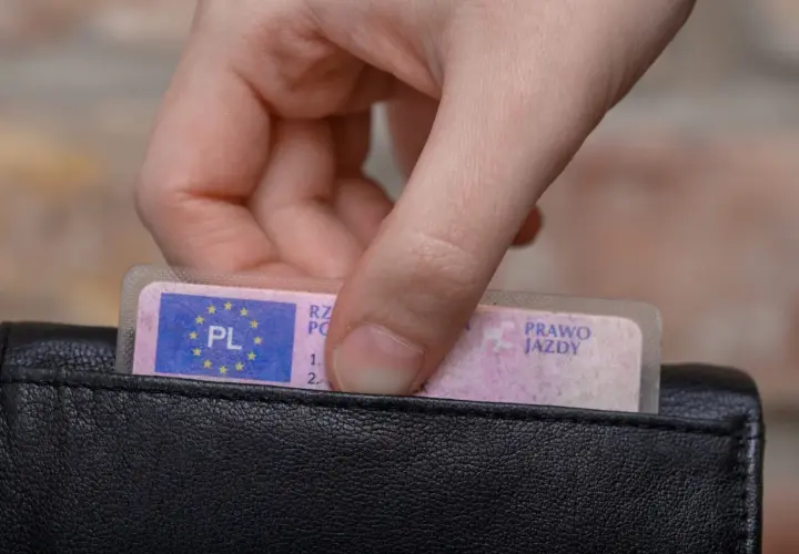Dłoń wkłada do czarnego portfela polskie prawo jazdy kategorii B.