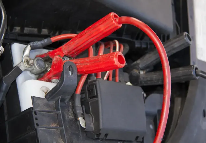 Czerwone kable rozruchowe podłączone do akumulatora. Zastanawiasz się, czy można odpalać auto przy podłączonym prostowniku?