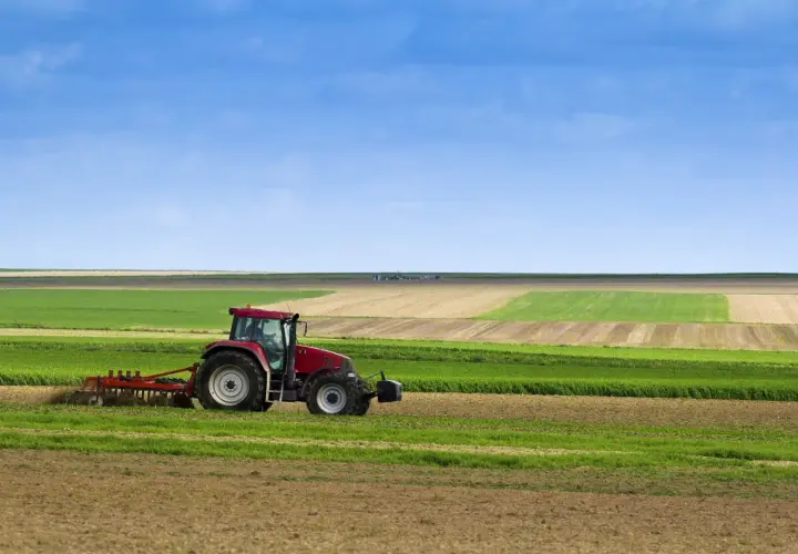 Tracteur rouge travaillant dans un champ, préparant le sol pour le semis direct. Paysage agricole sous un ciel bleu.