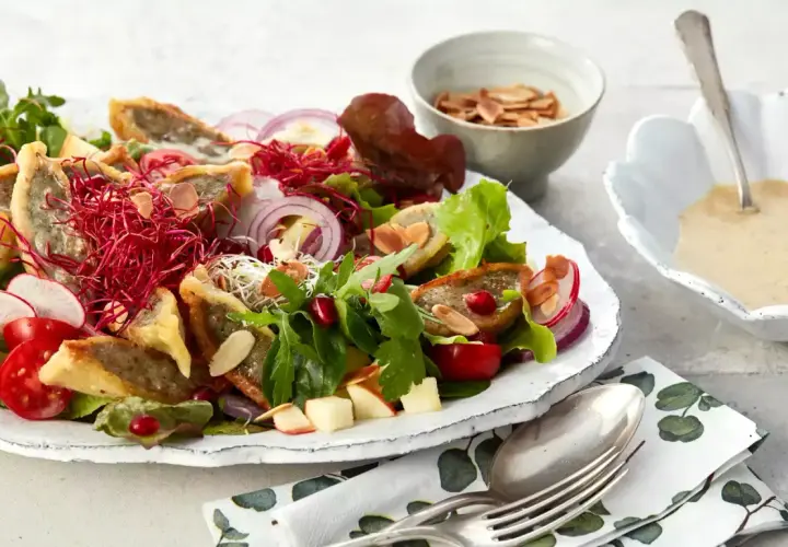 Herzhafter Maultaschen Salat mit knackigem Gemüse, roten Zwiebeln, Granatapfelkernen und Mandelsplittern. Dazu eine cremige Sauce.