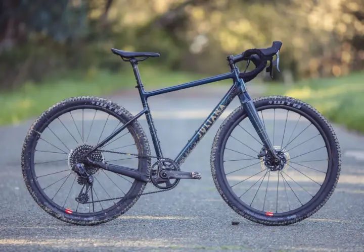 A dark blue Juliana gravel bike with gold lettering sits on a paved path, ready for adventure.