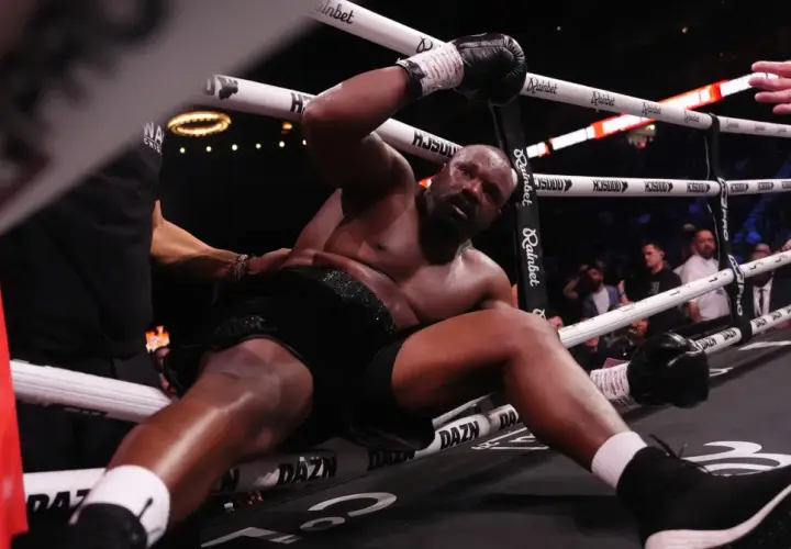 Derrick Chisora klęczy na macie, wyczerpany po walce. W tle widać publiczność i ring bokserski.
