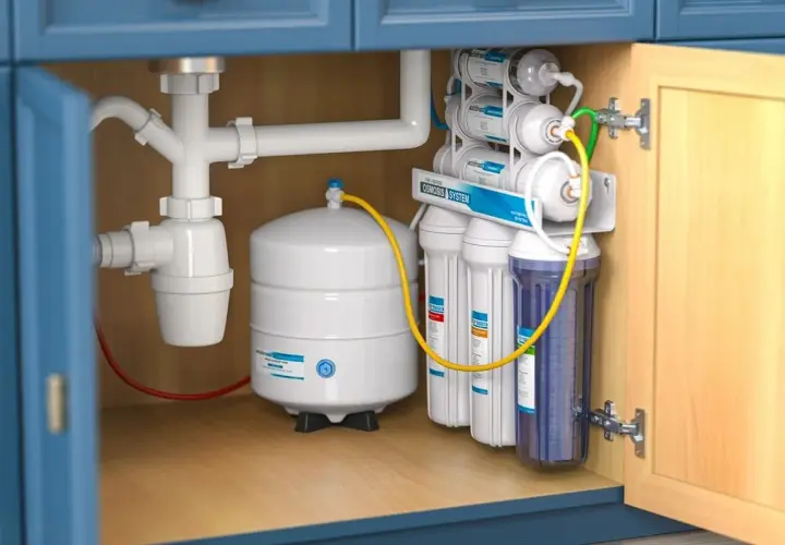 Montaż filtra do wody pod zlewem. System odwróconej osmozy z białym zbiornikiem i kilkoma przezroczystymi wkładami filtrującymi.