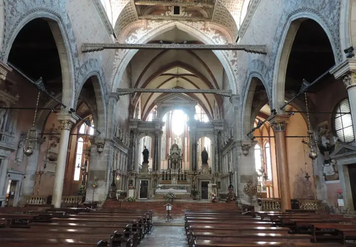 Intérieur de l'église Santo Stefano à Venise, avec ses bancs en bois, ses voûtes ornées et son autel baigné de lumière.
