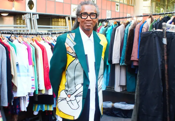 Man in a Bugs Bunny jacket stands by racks of colorful clothes, a testament to creative clothes upcycling.