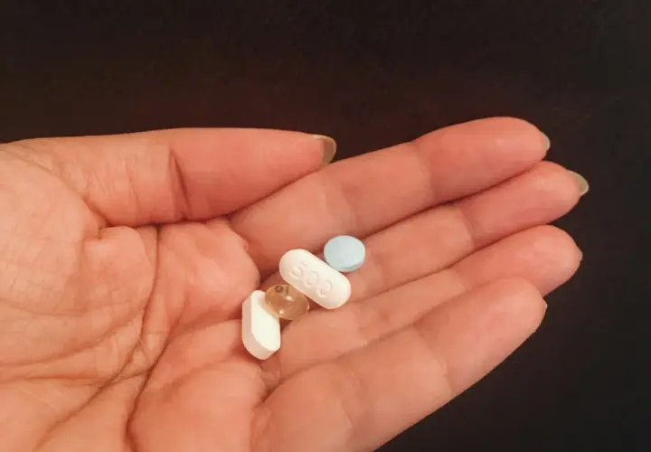 Dłoń trzyma kilka tabletek, w tym jedną z napisem "500". To może być wsparcie dla jelit, gdzie prebiotyk a probiotyk działają razem.