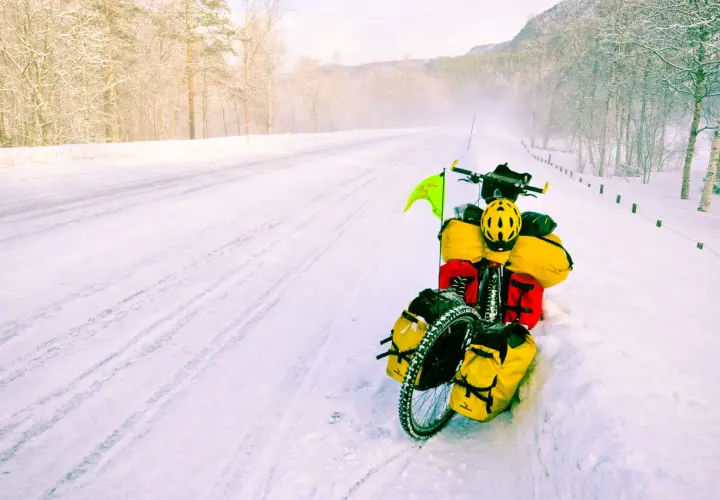 A fully loaded bicycle sits on a snowy road, a testament to adventure. The rider's concern about the brake fluid freezing point is evident in this winter scene.