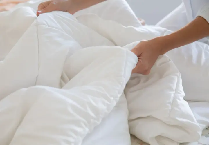 Hands smoothing a white duvet, a step in how to wash bedding for a fresh, clean sleep.