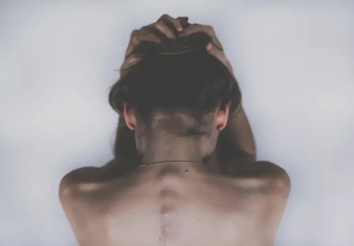 Vista posteriore di una persona con le mani tra i capelli, che evoca un senso di disagio legato alla rupofobia e alla sessualità.