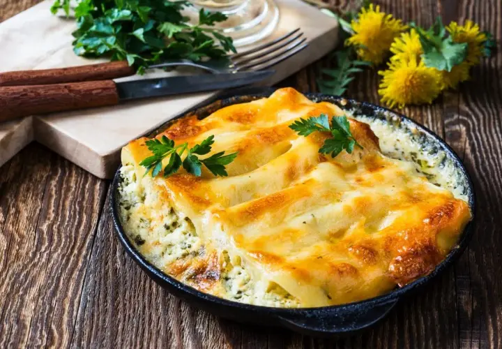 Zapiekane cannelloni w sosie, posypane serem i udekorowane natką pietruszki. Idealne danie na obiad.