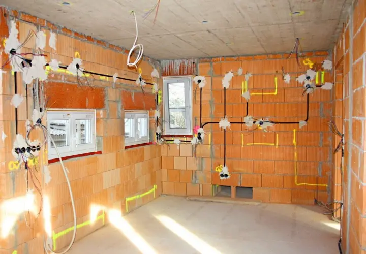 Schemat instalacji elektrycznej w nowym budynku. Widoczne przewody, puszki i oznaczenia na ścianach z cegły.