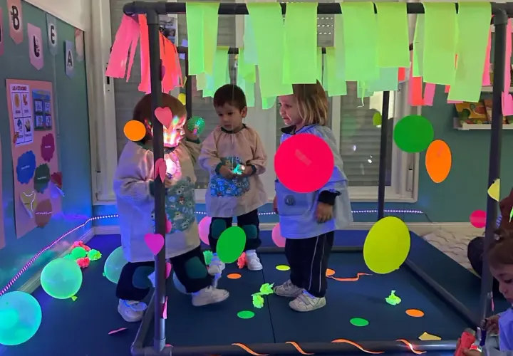 Niños explorando un aula multisensorial infantil con luces de neón, globos y elementos interactivos.