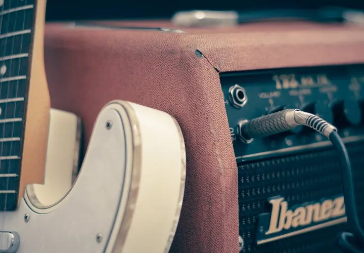 Biała gitara elektryczna podłączona do wzmacniacza Ibanez. Idealny zestaw, by dowiedzieć się, jak zacząć grać na gitarze elektrycznej.