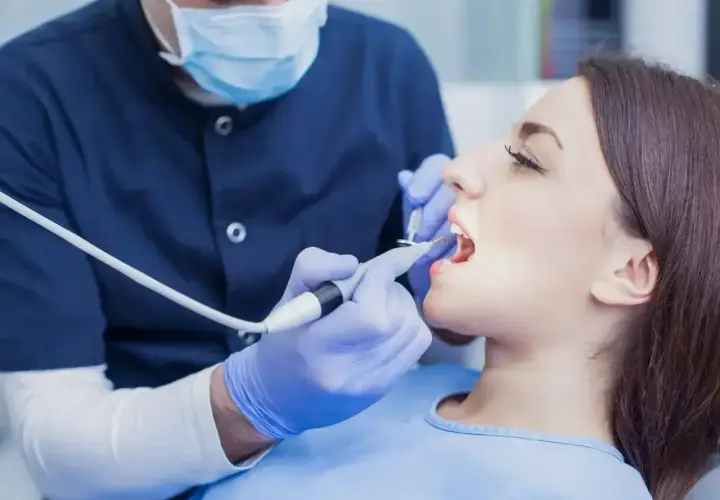 Dentysta w masce i rękawiczkach wykonuje zabieg. Zastanawiasz się, ile kosztuje znieczulenie u dentysty?