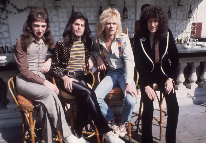 Freddie Mercury i zespół Queen siedzą przy barze w słoneczny dzień.