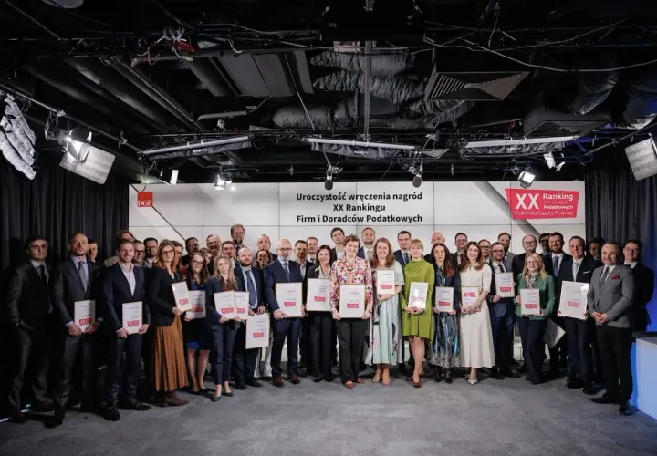 Grupa osób w garniturach i sukienkach pozuje do zdjęcia z nagrodami.
