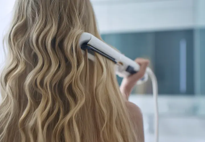 Kobieta kręci blond włosy lokówką, tworząc fale.