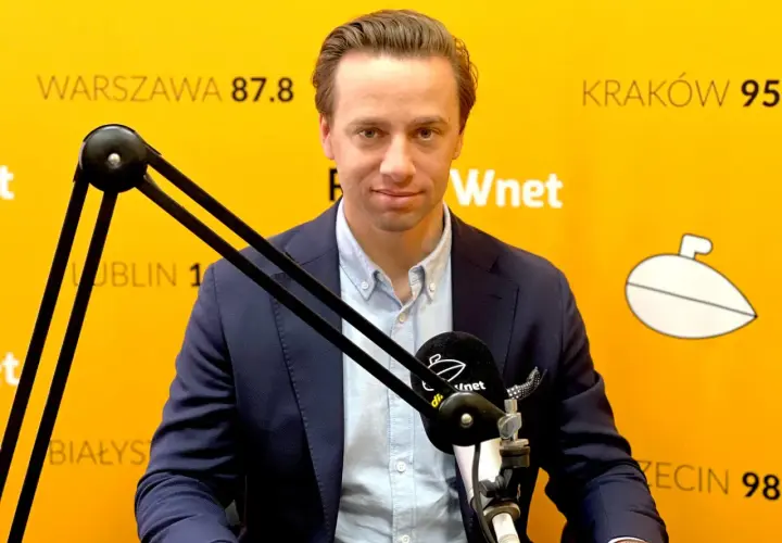 Krzysztof Bosak w garniturze przed mikrofonem na tle żółtej ściany z napisami.