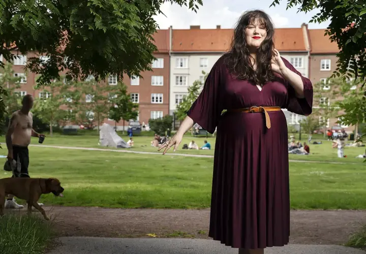 Maria Maunsbach i en vinröd klänning i en park med människor och en hund i bakgrunden.