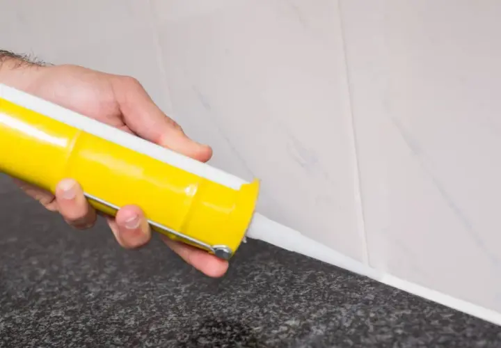Mano aplicando silicona blanca con pistola en juntas de azulejo. Guía práctica de como aplicar silicona en juntas para un acabado perfecto.